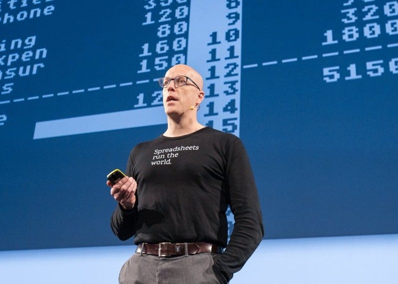 Hjálmar Gíslason on stage in a "Spreadsheets run the world" shirt, a retro VisiCalc-style budget projected behind him